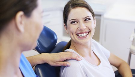 Woman in dental chair smiling up at dentist