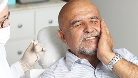 Man in dental chair holding his cheek